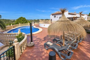 A swimming pool with a tiled deck, lounge chairs, and a thatched umbrella.