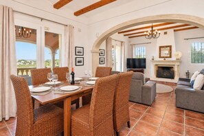 A dining area with a wooden table set for six, surrounded by wicker chairs.