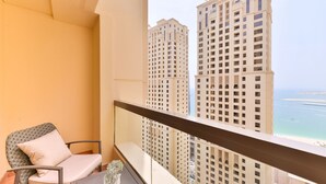 A balcony with a chair and a small table, overlooking tall buildings and a body of water.