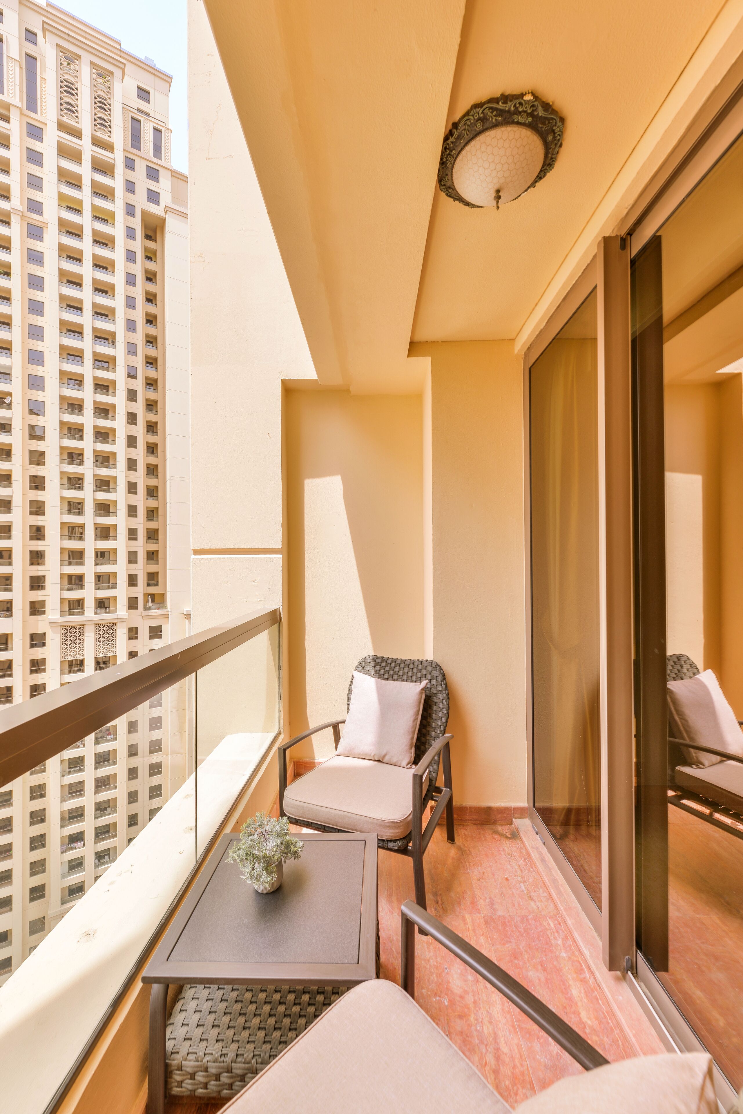 A balcony with a sofa, a small table with a plant, and a view of a tall building.