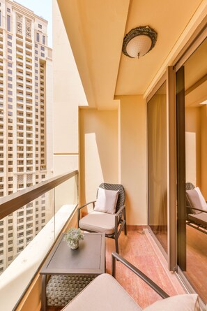 A balcony with a sofa, a small table with a plant, and a view of a tall building.