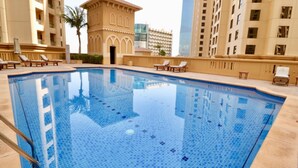 A swimming pool with tiled flooring, surrounded by lounge chairs and a palm tree.