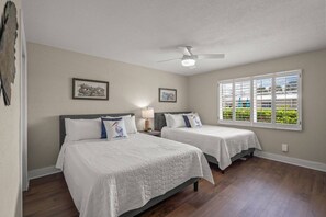 A bedroom with two beds, a ceiling fan, and a window with blinds.