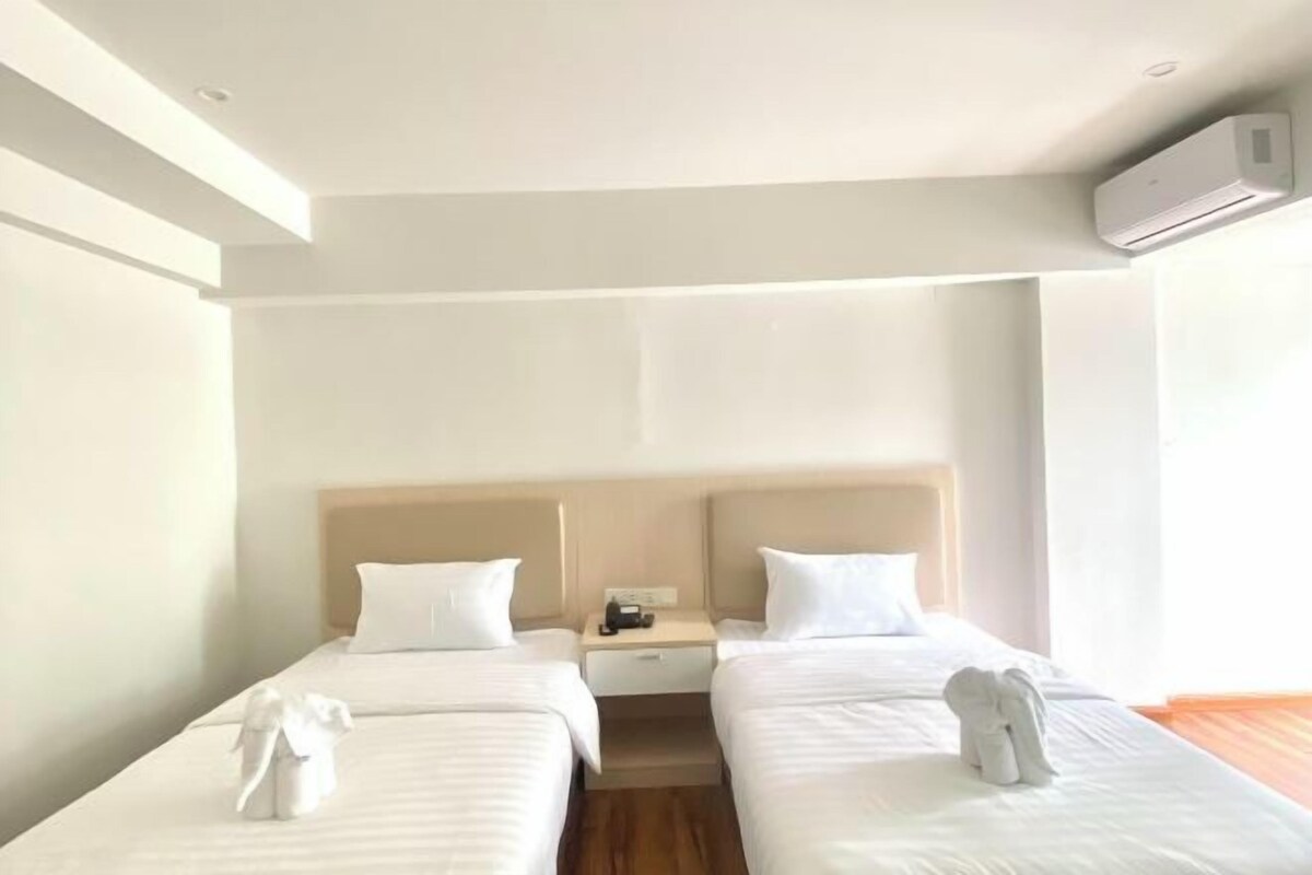 Quarto de hotel com duas camas de solteiro, chão de madeira, mesa de cabeceira com telefone e aparelho de ar condicionado.