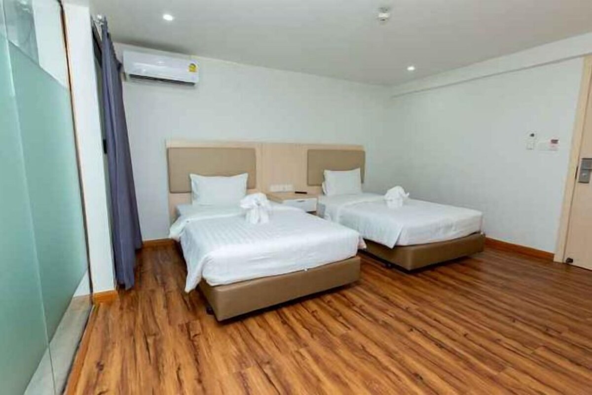 Quarto de hotel com duas camas, piso de madeira e janela com cortinas.