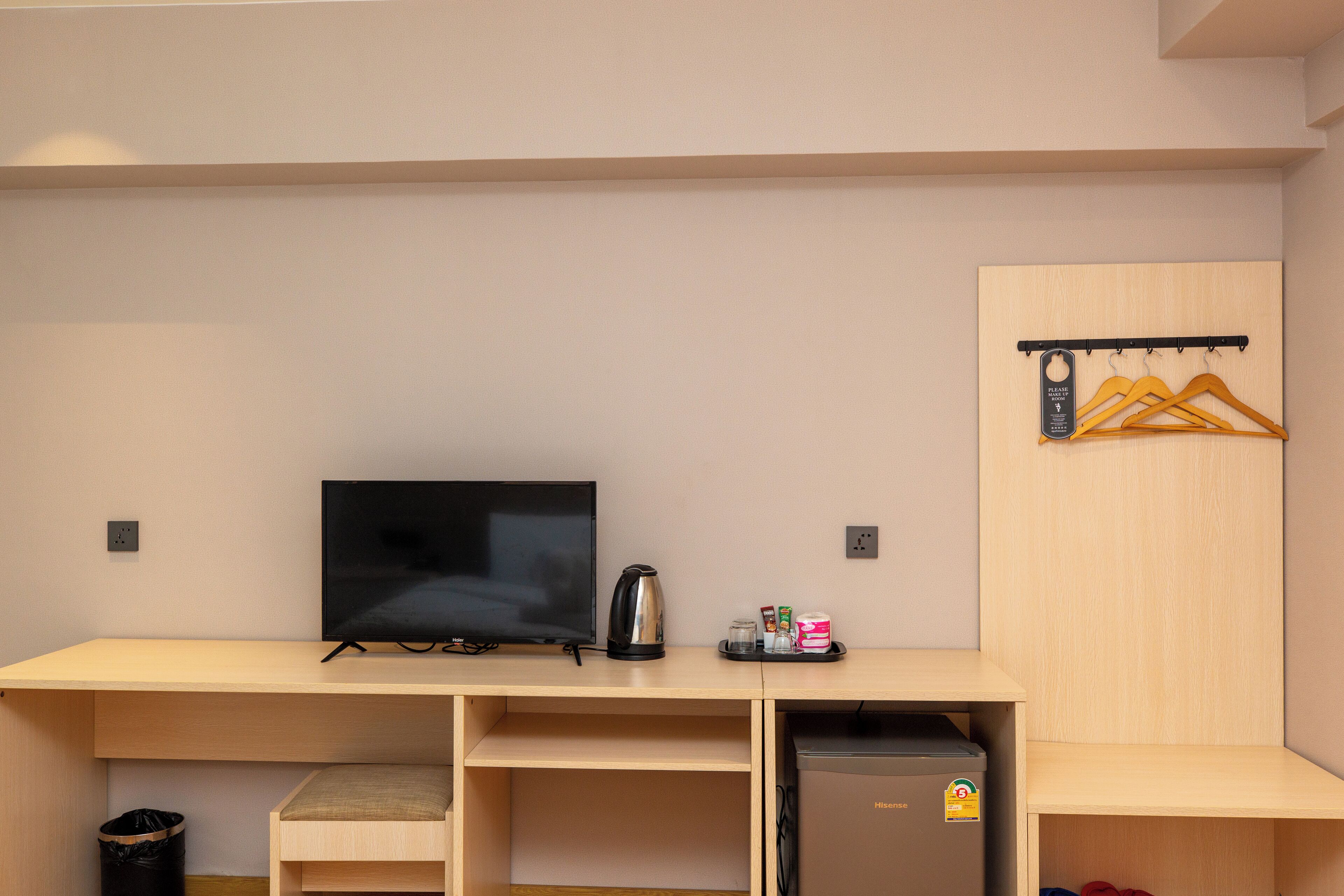 A hotel room with a TV, coffee maker, and a small refrigerator. There is a coat rack with hangers and a trash bin.