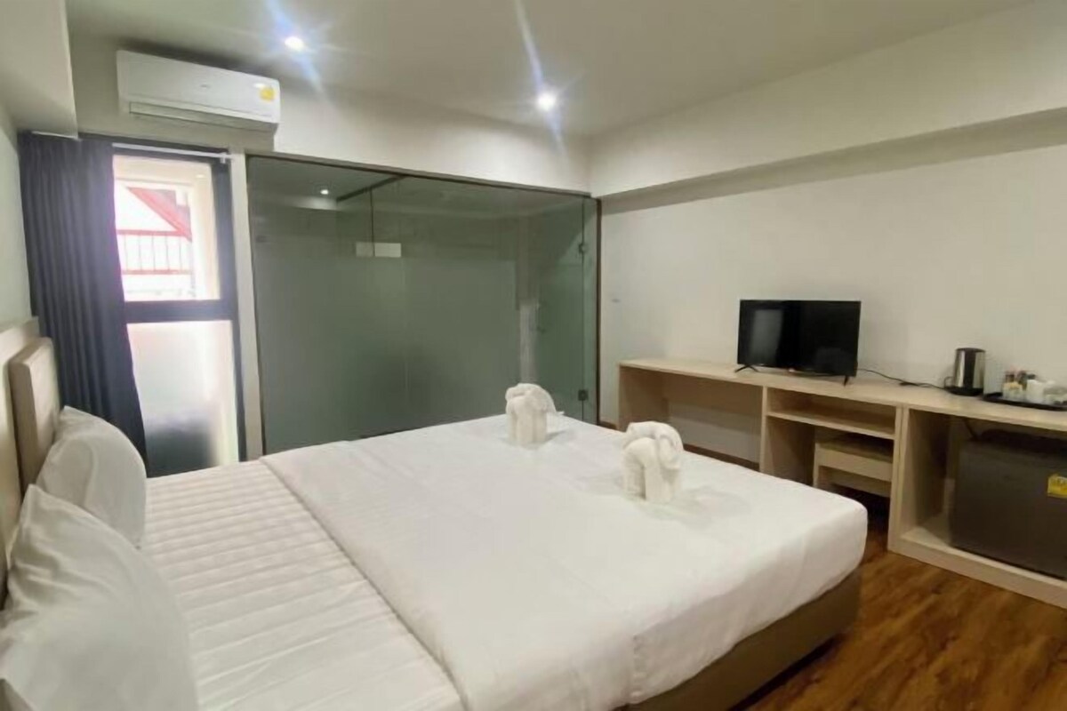 Quarto de hotel com cama, televisão, escrivaninha e porta de vidro para uma varanda.