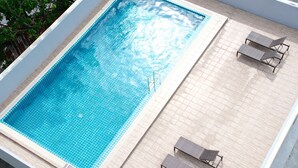 A rectangular swimming pool with clear blue water, surrounded by a tiled deck. There are two lounge chairs on the deck. - lucky Elephant Hotel (Bangkok)