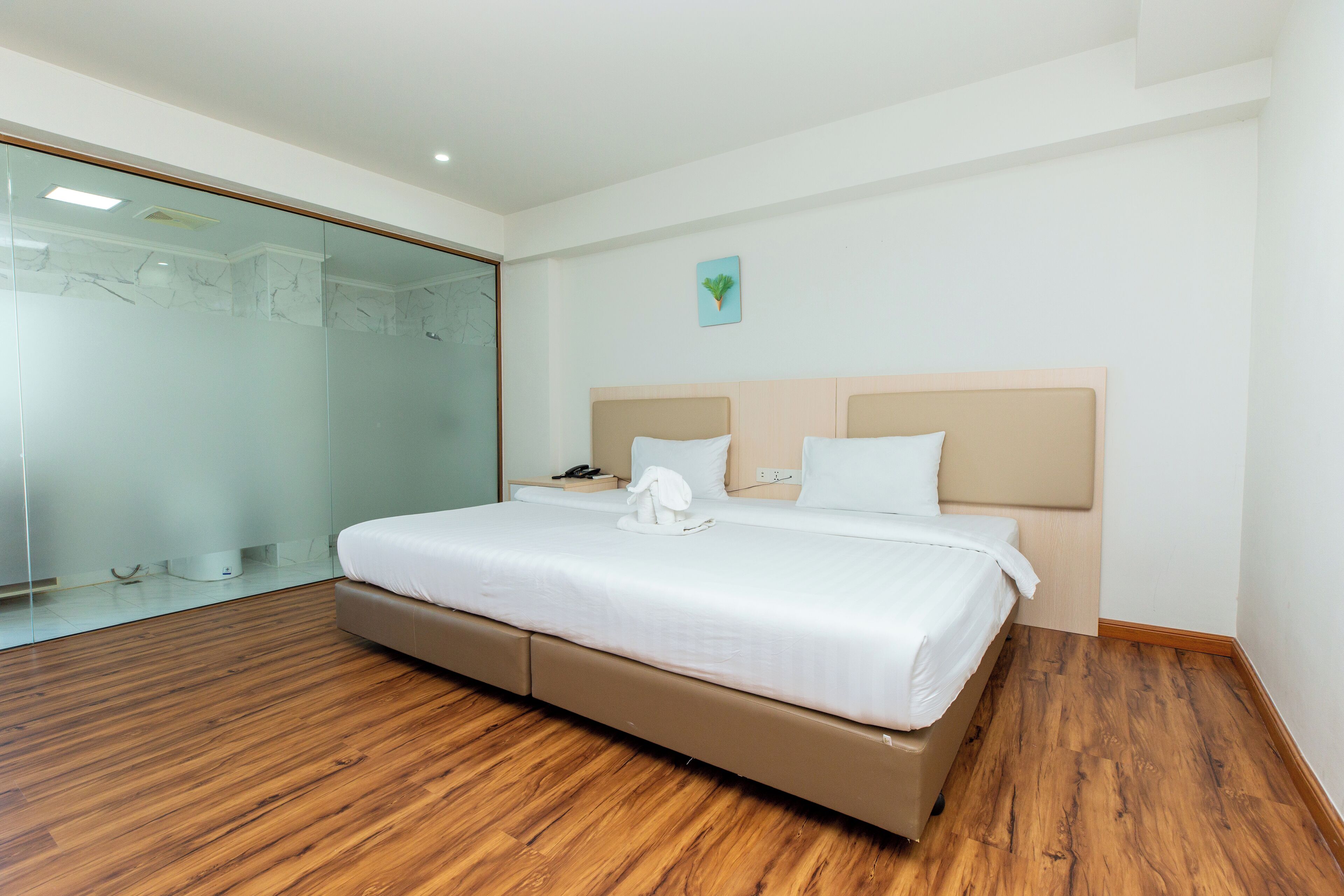 A modern hotel room with a large bed, wooden flooring, a glass shower enclosure, and a small artwork on the wall.
