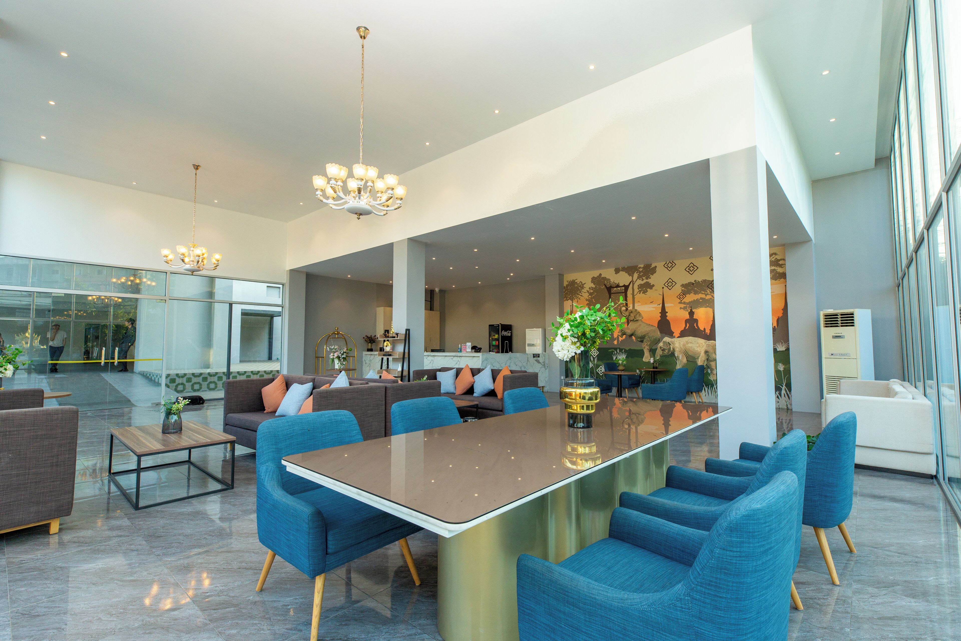 A spacious living area with a large central table, blue upholstered chairs, and a chandelier.
