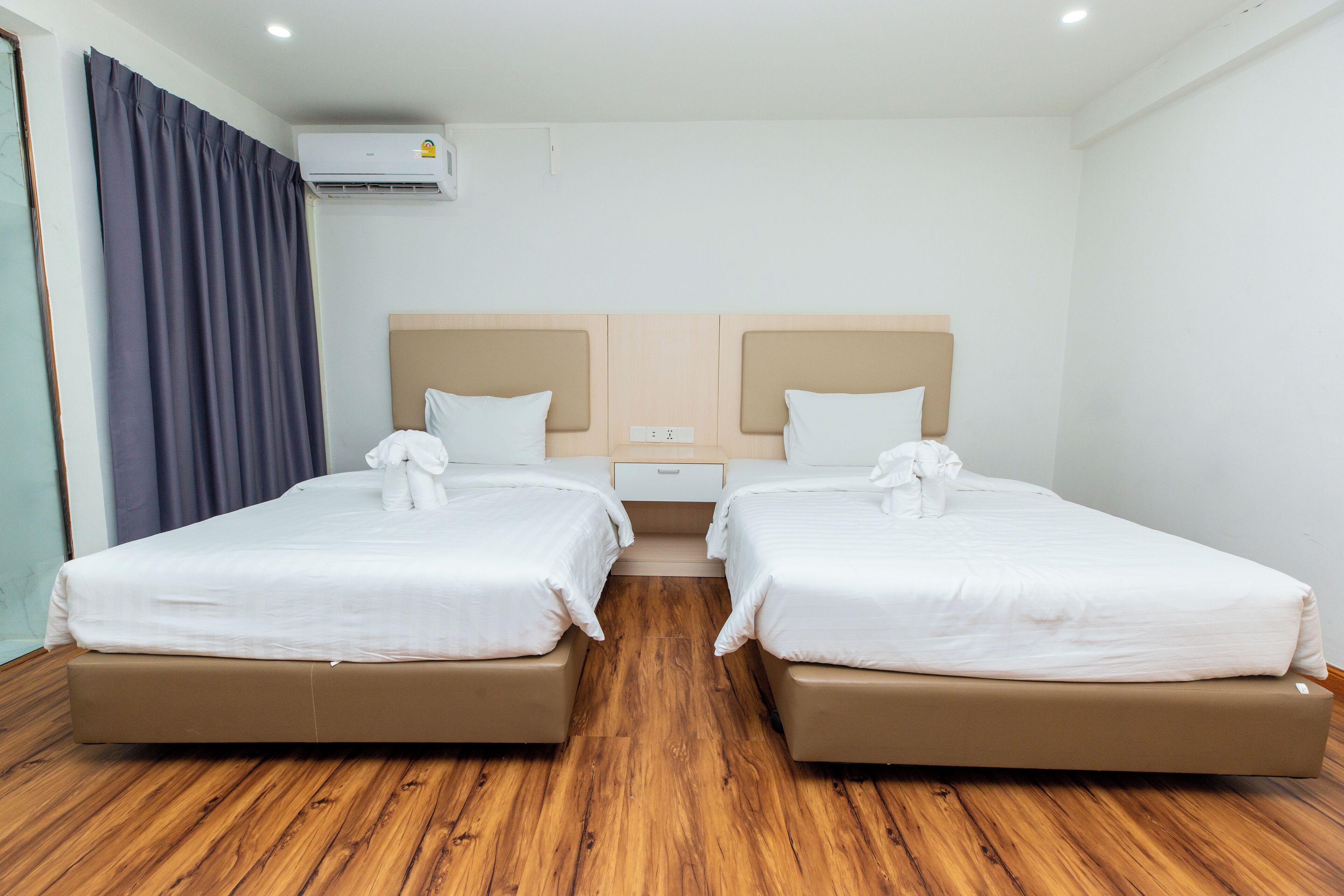 Une chambre d’hôtel avec deux lits, un plancher en bois, un climatiseur au plafond et une fenêtre avec des rideaux.