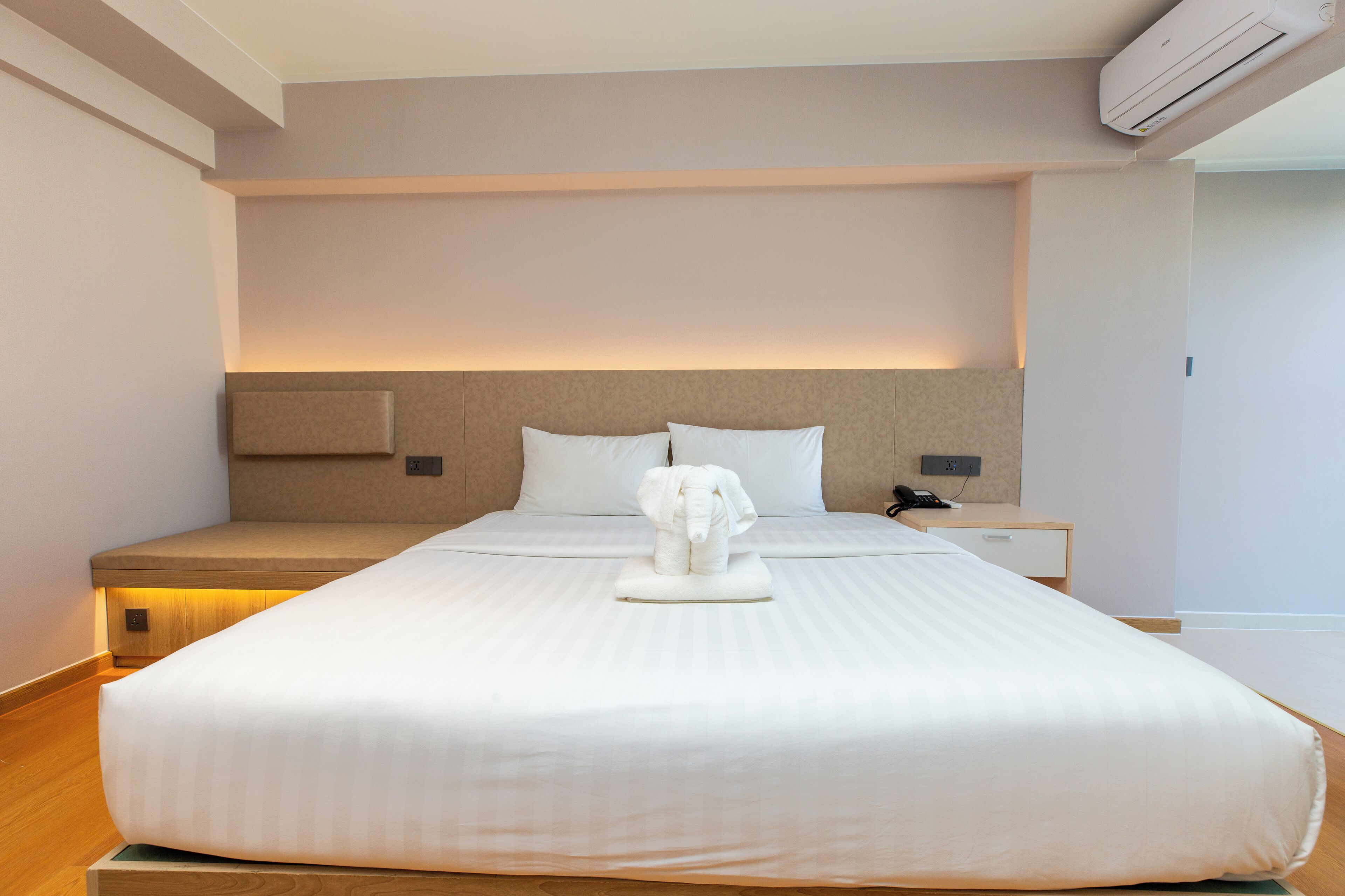 A hotel room with a large bed, a bedside table, an air conditioning unit, and a nightstand.