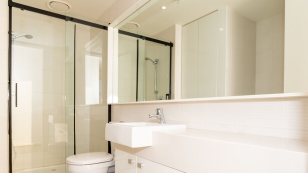 Een moderne badkamer met een douchecabine van glas, een wit toilet en een grote spiegel boven een witte wastafel.