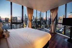 Habitació d'hotel amb vistes a la ciutat, un llit gran i dues finestres amb cortines.