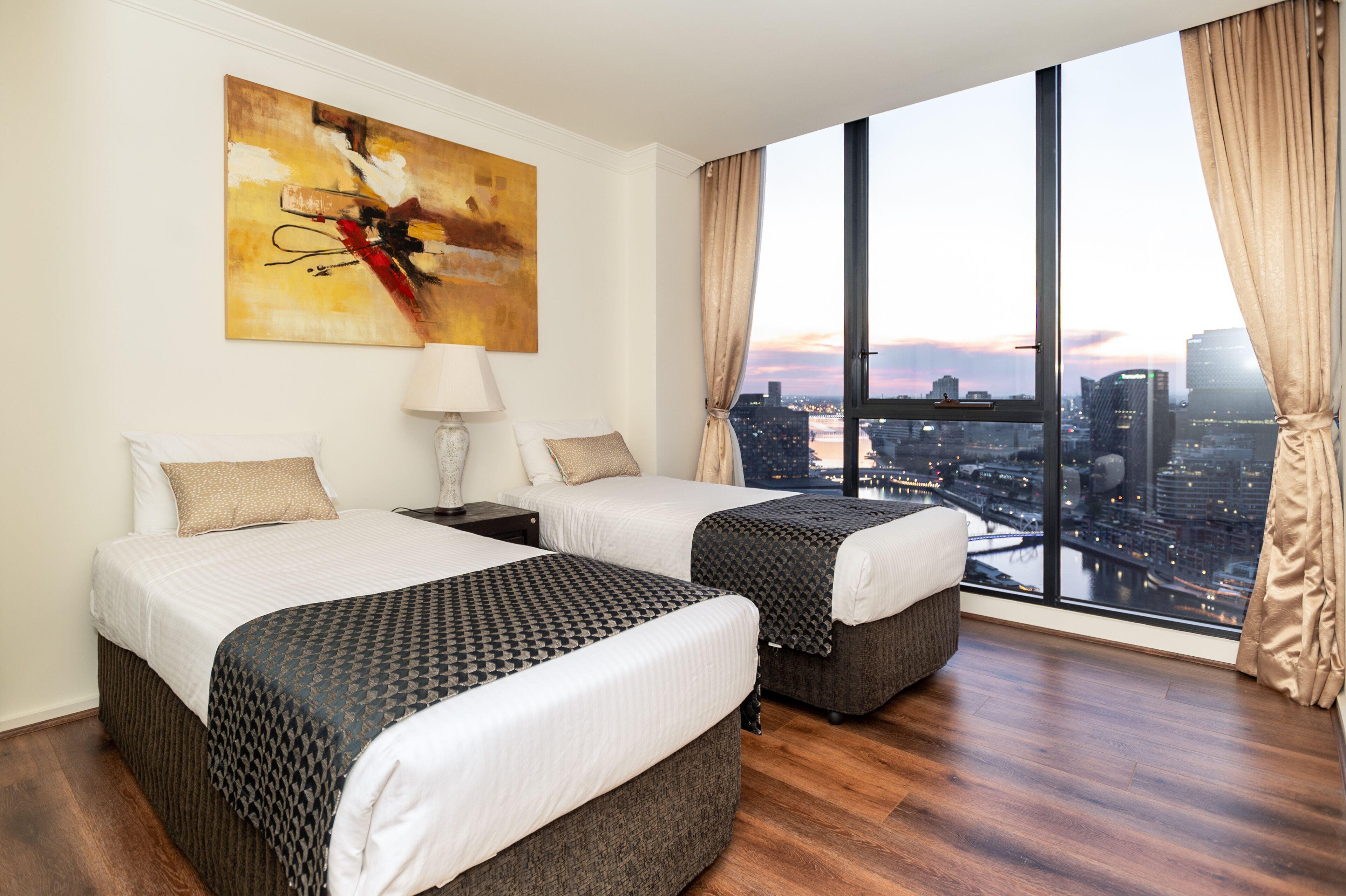A hotel room with two beds, a city view, and a large abstract painting on the wall.
