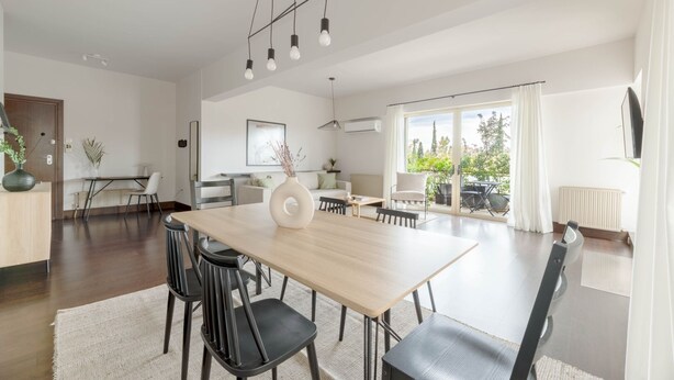 Et moderne spiseområde med et stort træbord, sorte stole og en hvid vase som midtpunkt.