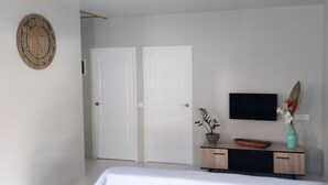 Une chambre à coucher avec un lit, une commode en bois sur laquelle se trouve un téléviseur, une horloge et deux portes.