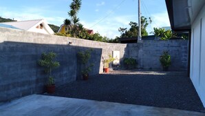 Un mur en béton agrémenté de plantes en pot, une zone recouverte de gravier et un bâtiment en arrière-plan.
