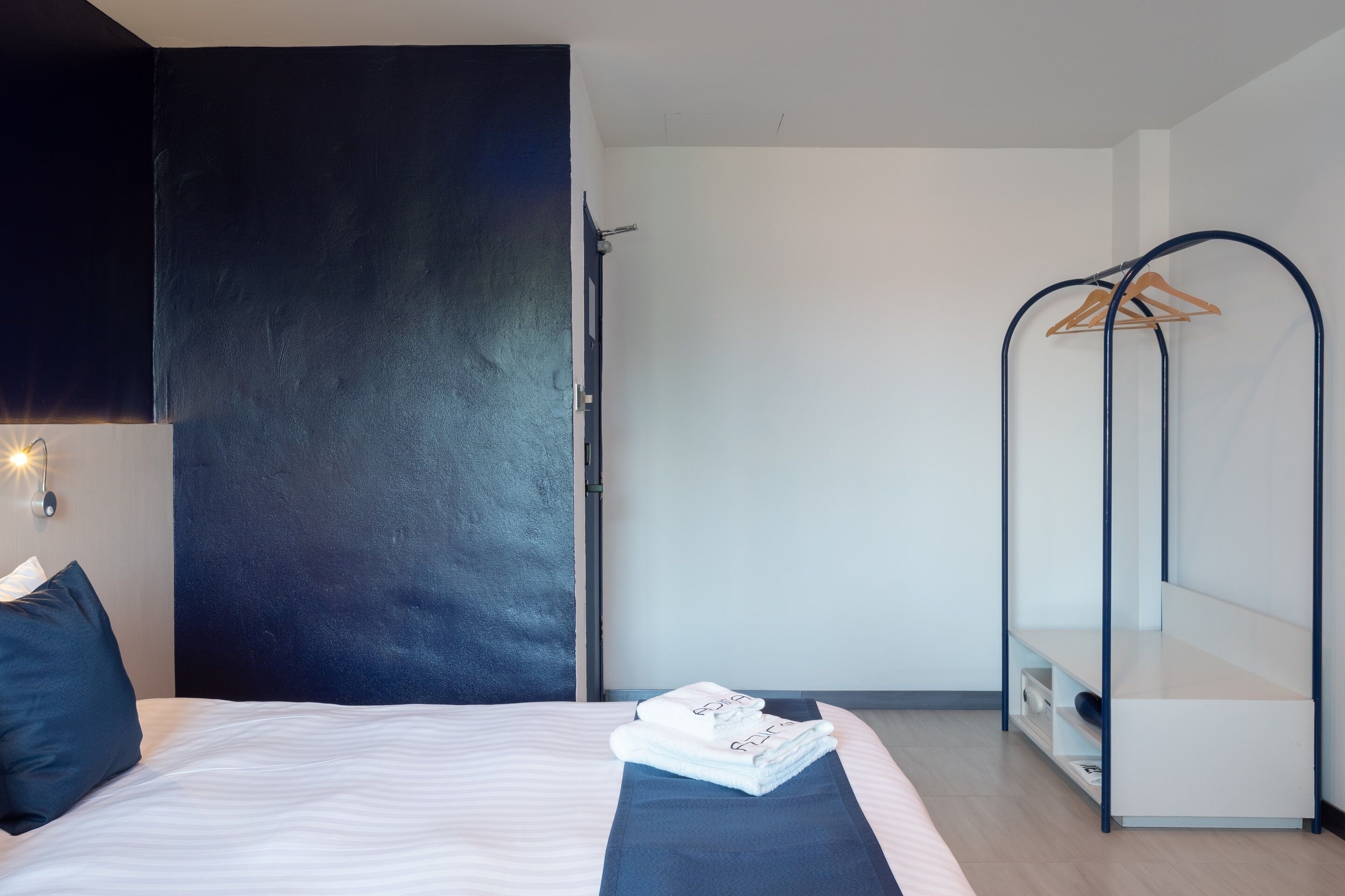 A modern hotel room with a bed, a dark wall, a white wardrobe, and a hanging clothes rack.
