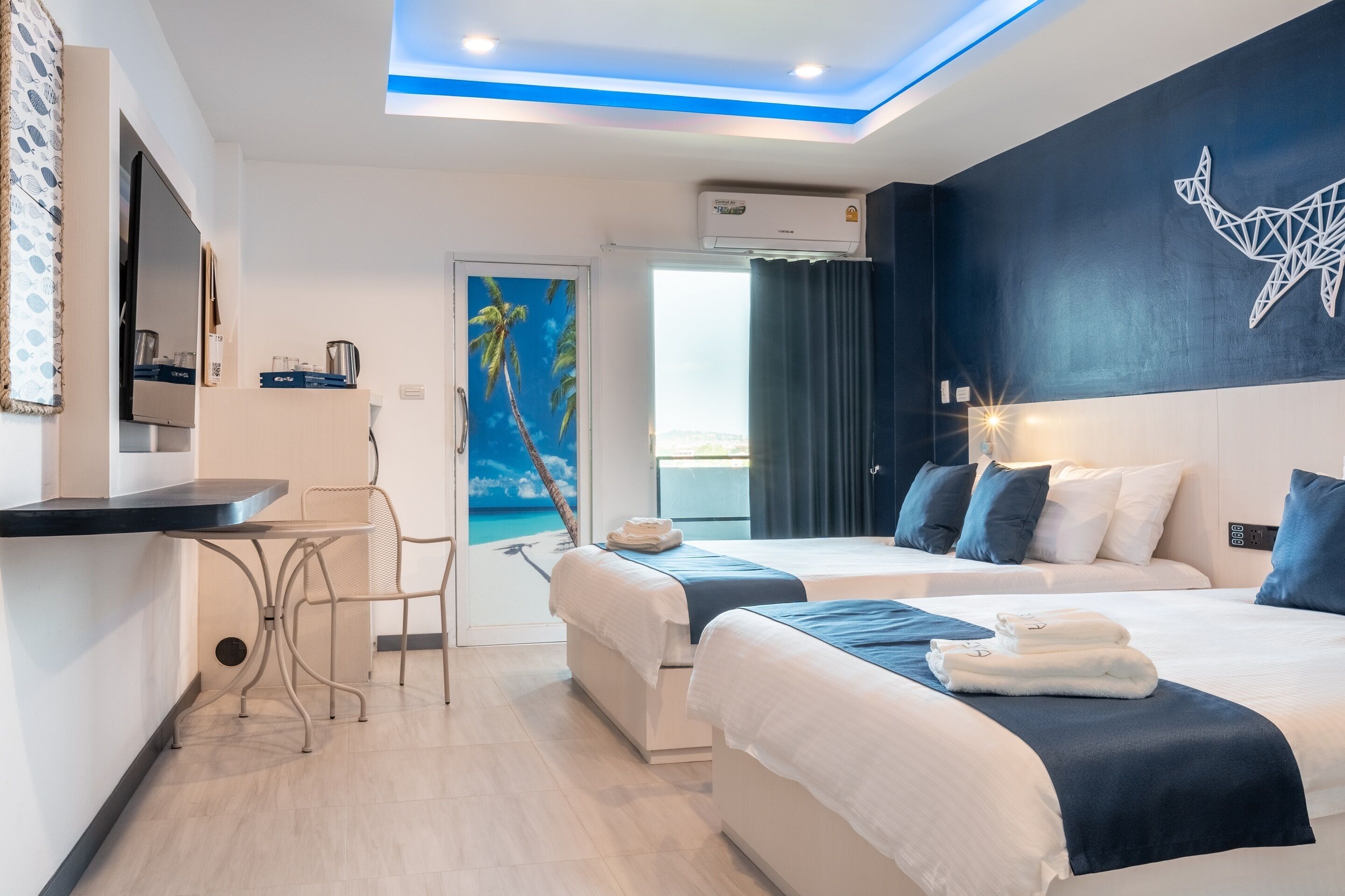 A hotel room with two beds, a desk, and a painting of a beach scene.