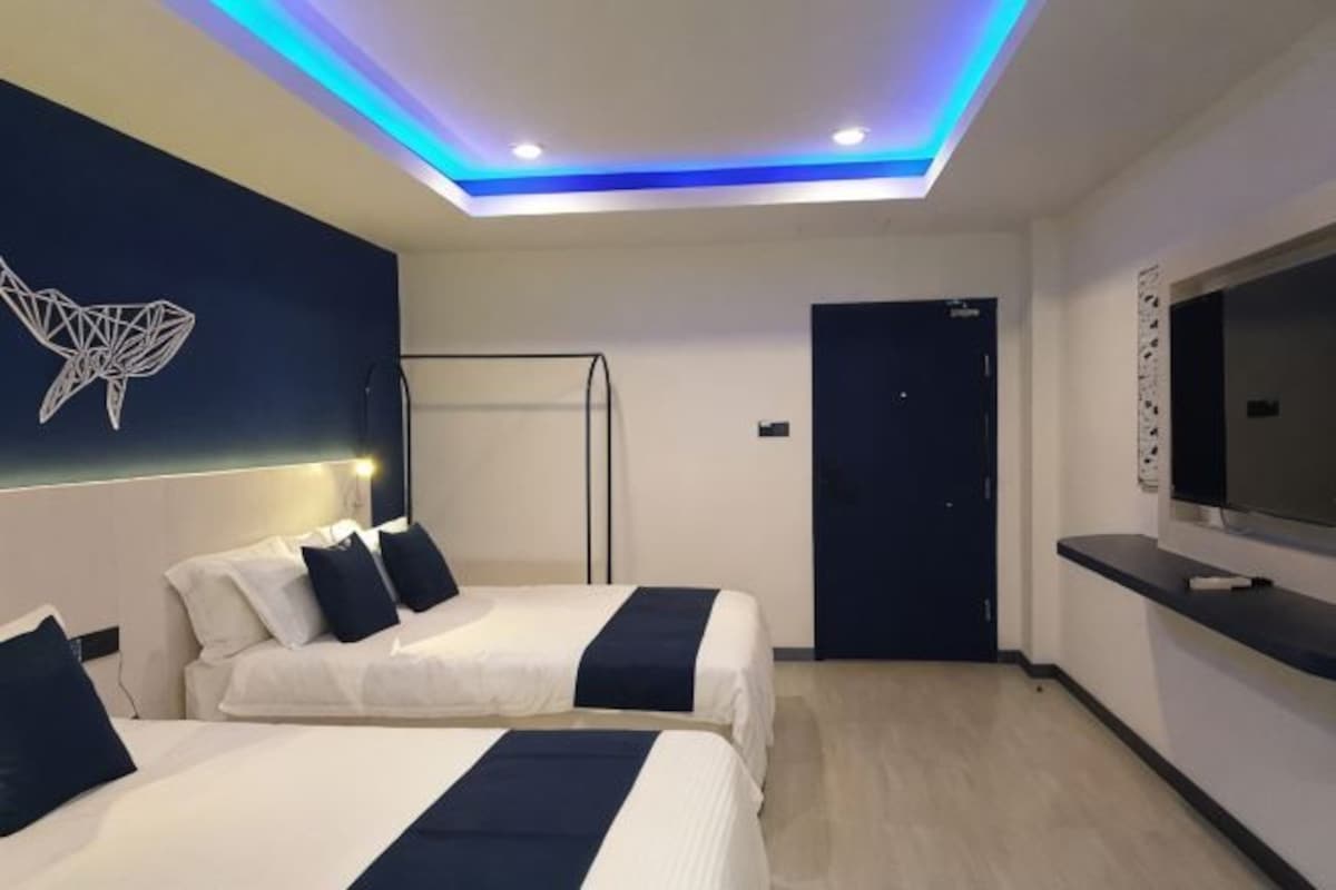 A modern hotel room with two beds, a flat-screen TV, and a ceiling light fixture.