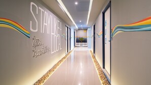 Um corredor de hotel moderno com um letreiro 'STAYLIKE LOCAL', piso limpo e vista para o exterior.