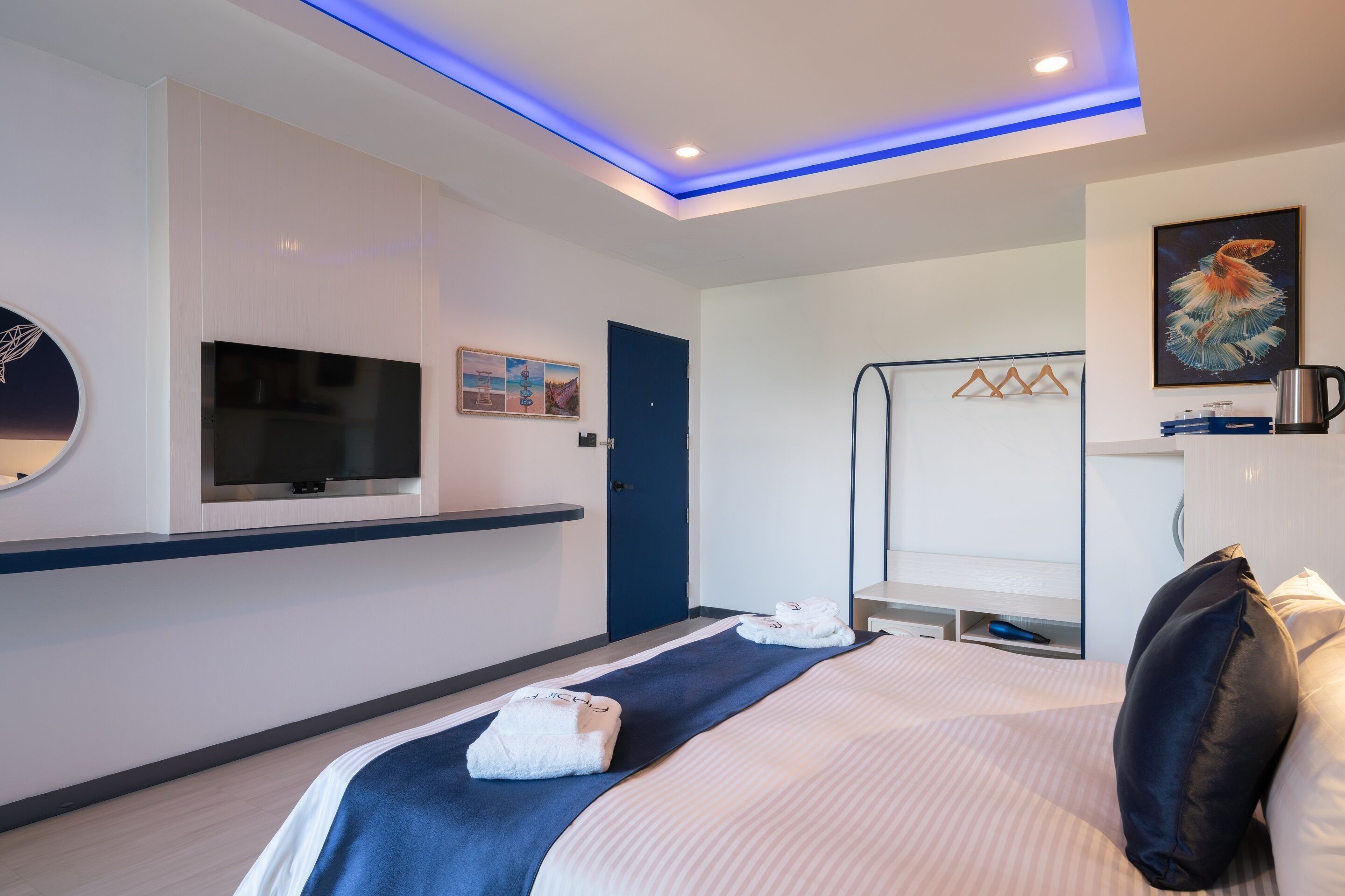 A modern hotel room with a large bed, a flat-screen TV, a painting, and a blue-lit ceiling.