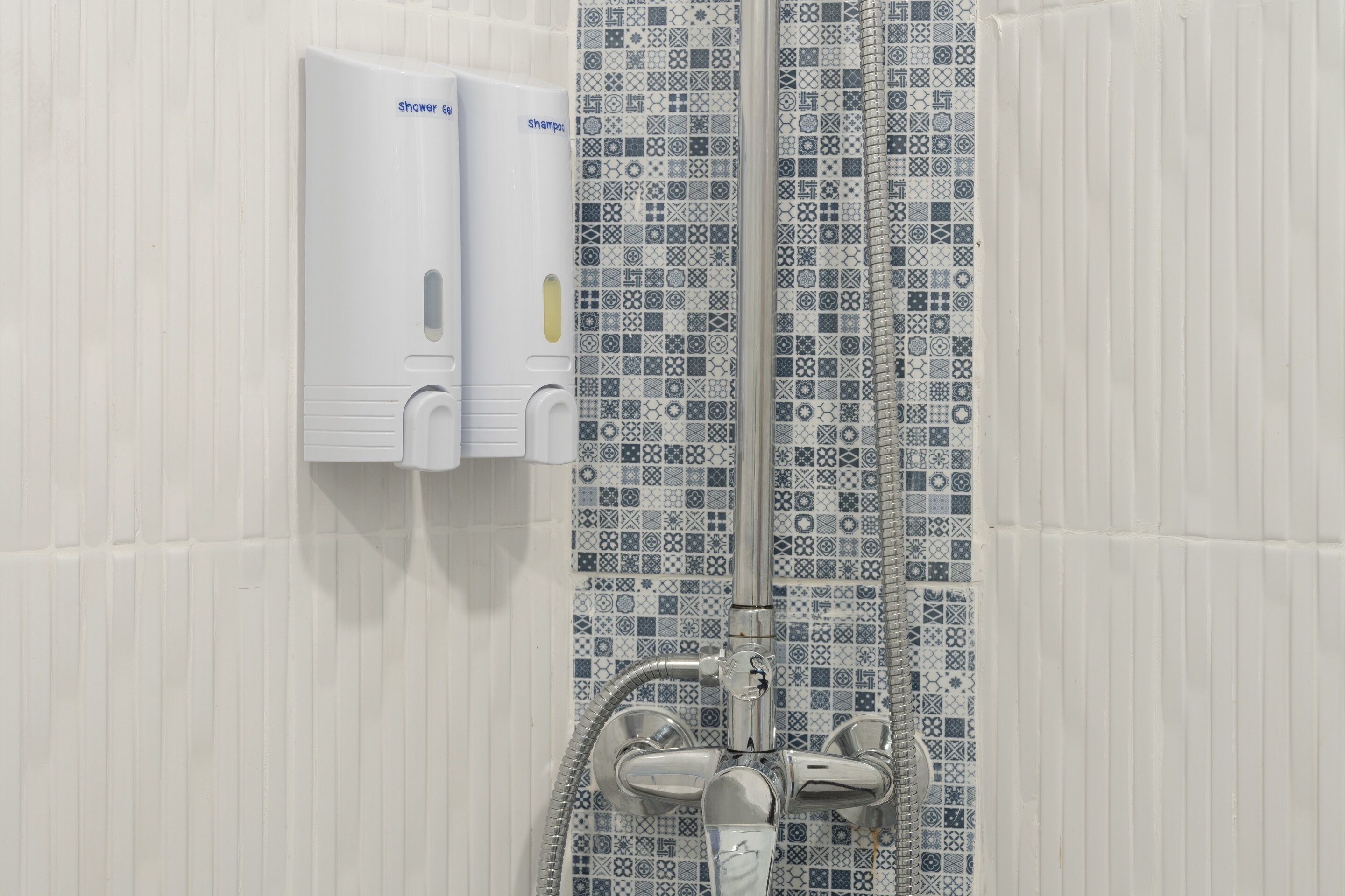 Zona de ducha con pared de azulejos estampados, un secamanos y un cabezal de ducha.
