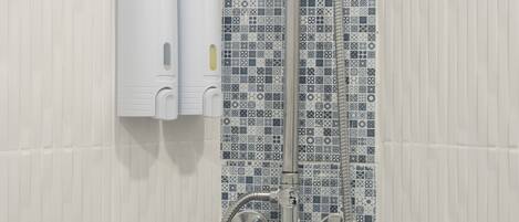 Zona de ducha con pared de azulejos estampados, un secamanos y un cabezal de ducha.