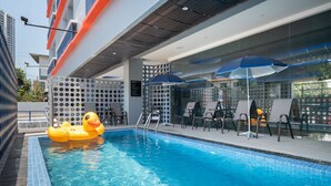 Piscina com boia de pato, cadeiras de descanso e guarda-sóis.