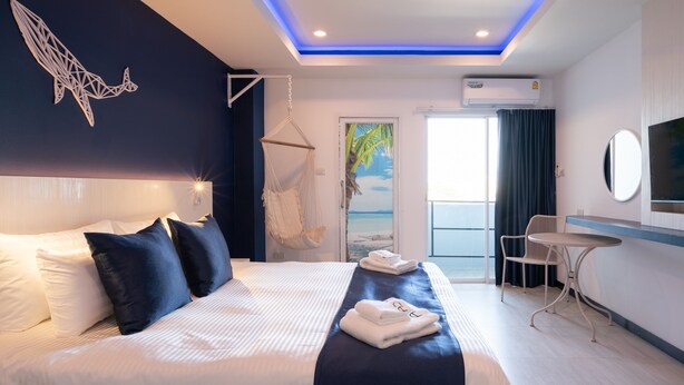 Quarto de hotel moderno com cama, uma cadeira suspensa, uma pequena mesa e vista para o mar pela porta.
