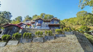 A multi-story house with a stone facade and multiple balconies, surrounded by trees and a clear sky. - Kamlia 3 BHK Villa By Dumnu Homes (Kasauli)