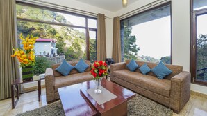 A spacious living room with two brown sofas, a coffee table, and a large window offering a view of a hillside. - Kamlia 3 BHK Villa By Dumnu Homes (Kasauli)