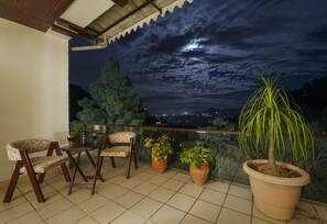 A balcony with two chairs, two potted plants, and a view of a cityscape at night. - Kamlia 3 BHK Villa By Dumnu Homes (Kasauli)