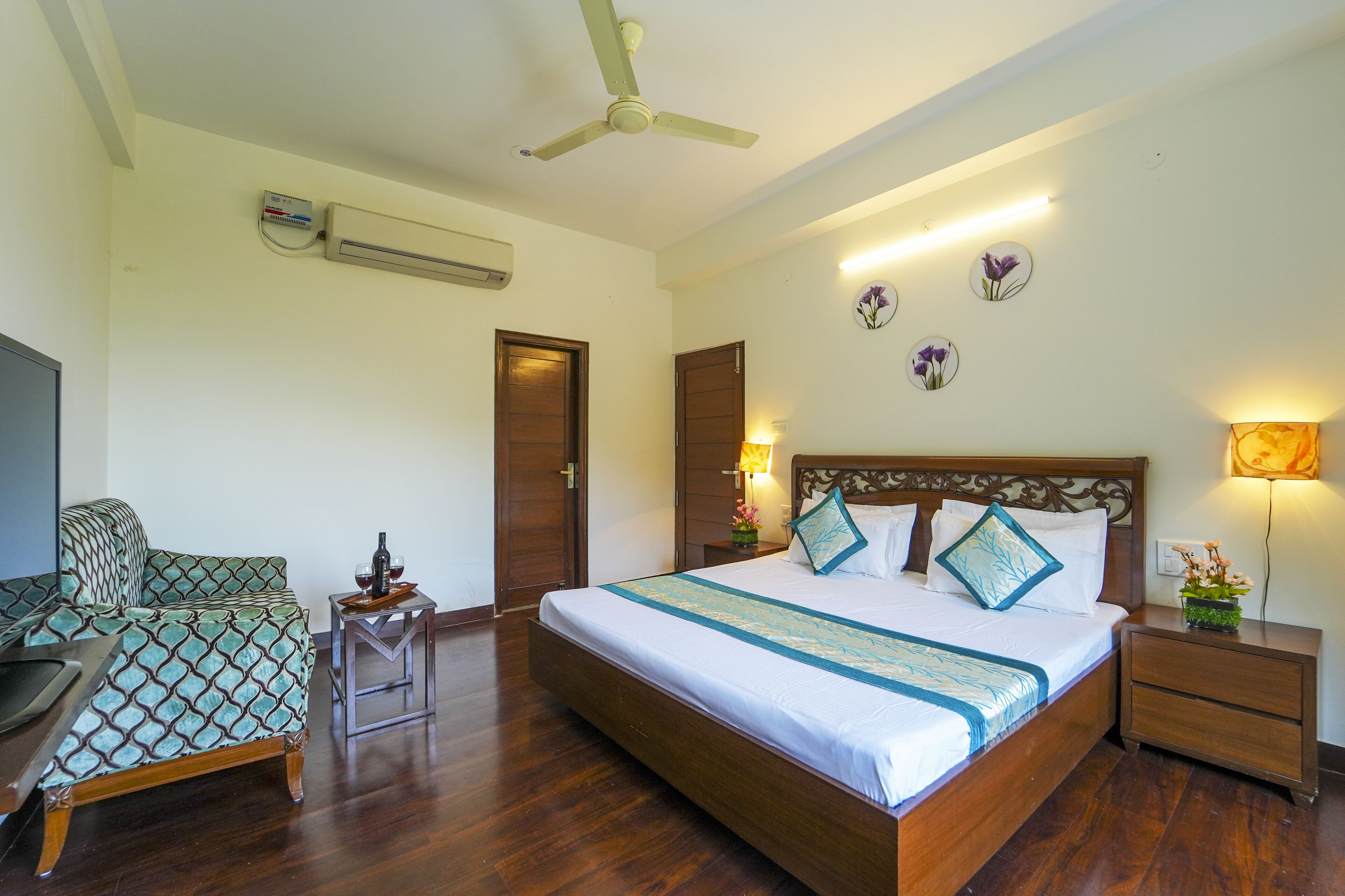 A hotel room with a large bed, a desk, a chair, a ceiling fan, and a wall-mounted air conditioner.