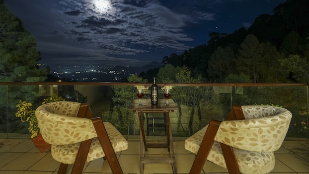 A balcony with a table and two chairs, a bottle, and two glasses of red wine. - Kamlia 3 BHK Villa By Dumnu Homes (Kasauli)