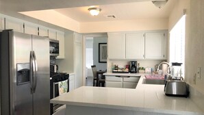 A modern kitchen with white cabinetry, a stainless steel refrigerator, a coffee maker, and a blender.
