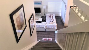 A staircase leading to a living room with a sofa, TV, and framed pictures on the wall.