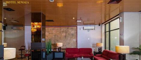 A hotel lobby with a wooden ceiling, red sofas, and a glass partition.