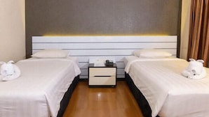 Habitación de hotel con dos camas individuales, una mesita de noche con lámpara y una cortina en la ventana.