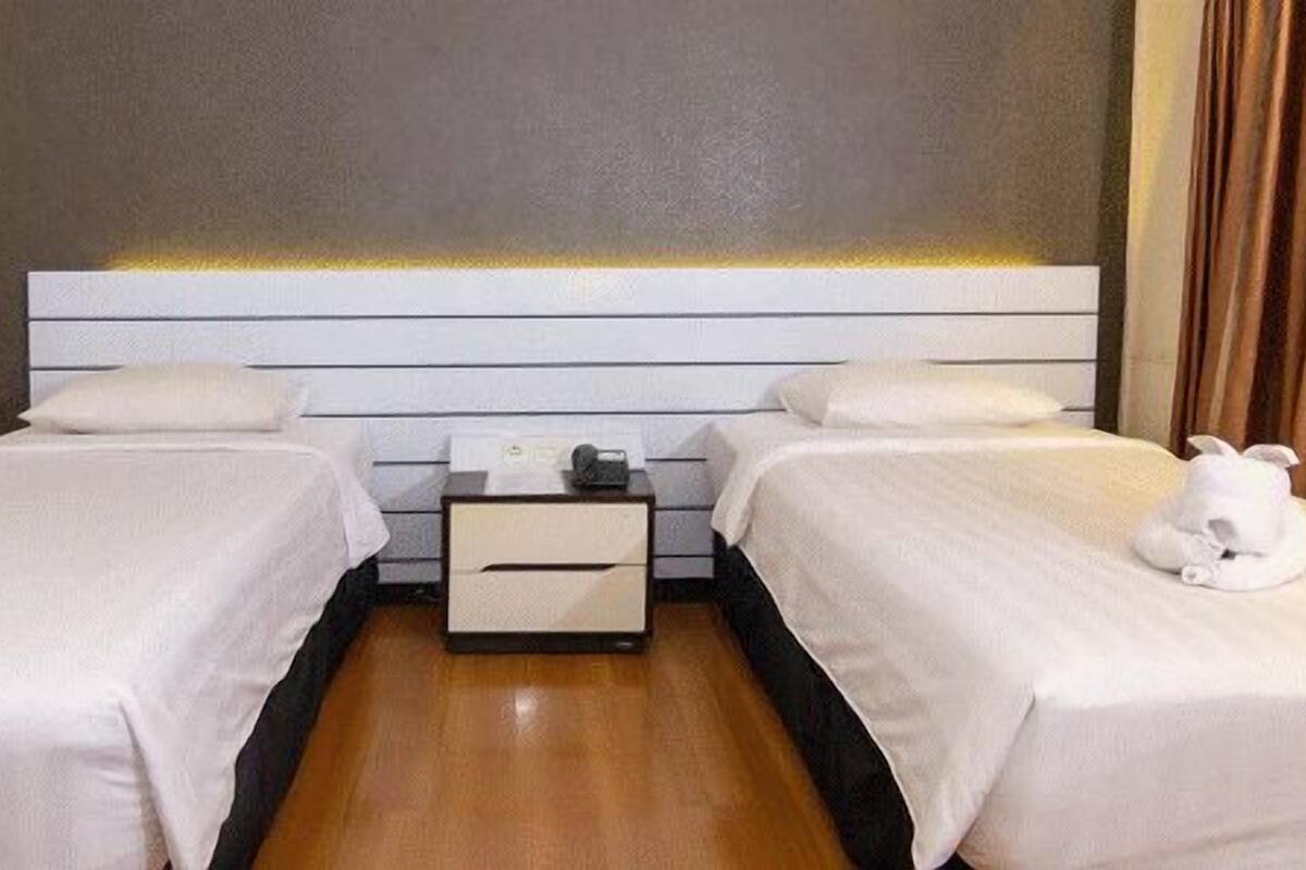 A hotel room with two single beds, a nightstand with a lamp, and a curtain on the window.