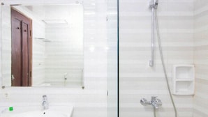 Un baño con lavamanos, espejo, ducha y mampara de vidrio.