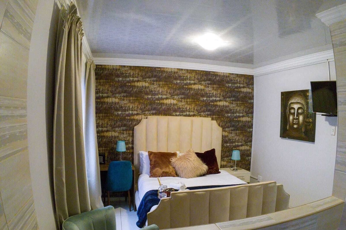 A hotel room with a bed, a chair, a desk, and a wall-mounted TV.