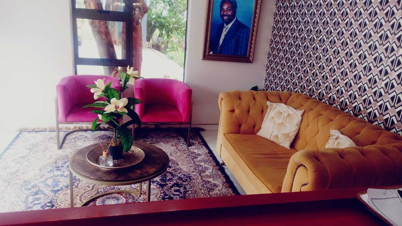 Una habitación con un sofá amarillo, una silla rosa y una mesa redonda con un jarrón de flores.