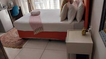 A bedroom with a bed, bedside table, and a small window with curtains.