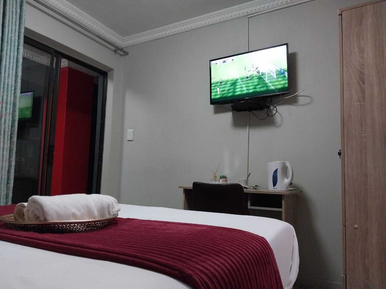 Una habitación de hotel con cama, televisión montada en la pared, escritorio y armario.