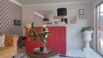 A living room with a sofa, a round table with a potted plant, a red partition, a white pedestal, and a large window.