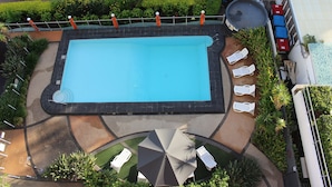 Vue aérienne d’une piscine avec des chaises longues et un espace de détente abrité.