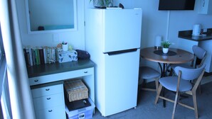 Une petite cuisine équipée avec un réfrigérateur blanc, une petite table à manger avec deux chaises, une plante en pot et un téléviseur à écran plat fixé au mur.