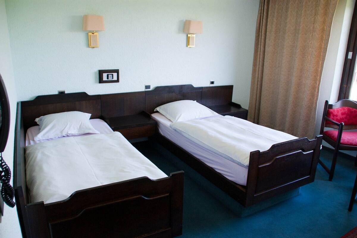 A hotel room with two single beds, bedside lamps, a small table, and a chair.